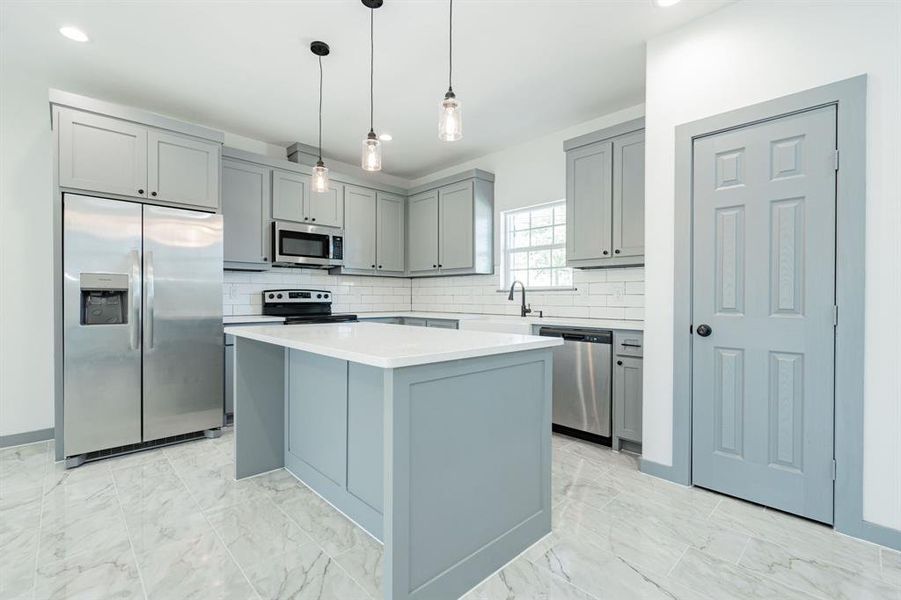 Kitchen with light tile patterned flooring, appliances with stainless steel finishes, backsplash, and a kitchen island