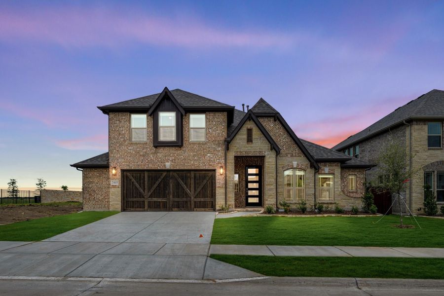 Two-story brick home with dark wood garage doors, arched entry, and manicured front lawn at dusk