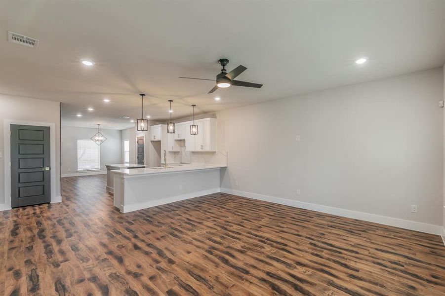 Kitchen with kitchen peninsula, ceiling fan with notable chandelier, white cabinets, dark hardwood / wood-style floors, and hanging light fixtures