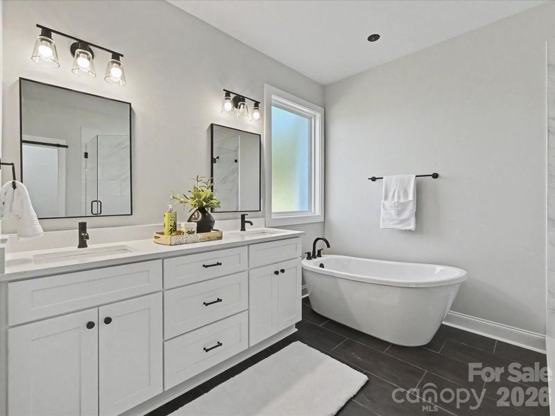 Luxurious primary bath features dual vanities, a freestanding soaking tub, and an oversized tiled walk-in shower with sleek modern finishes.