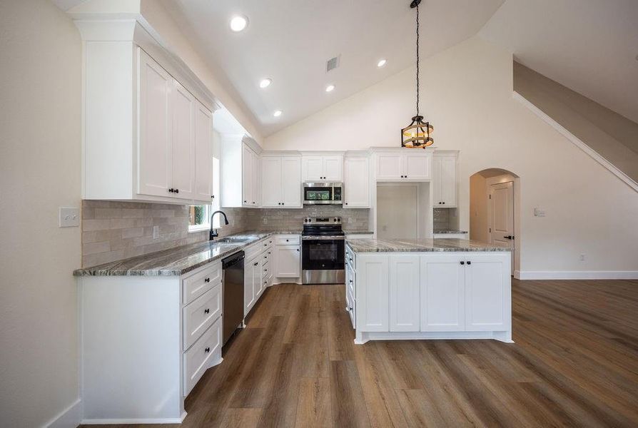 Kitchen with white cabinetry, arched walkways, stainless steel appliances, a center island, and tasteful backsplash