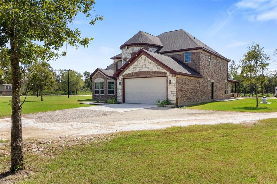 This photo showcases a spacious two-story brick home with a stone facade, featuring a two-car garage. It's situated on a large, grassy lot with mature trees, providing a serene and private setting.