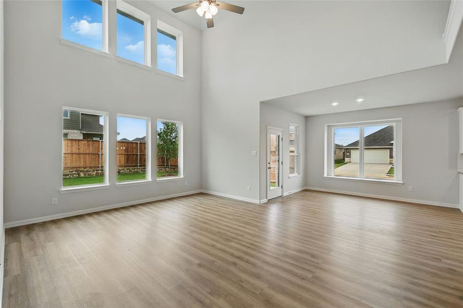 Unfurnished living room featuring wood finished floors, ceiling fan, baseboards, and a high ceiling Unfurnished living room featuring wood finished floors, ceiling fan, baseboards, and a high ceiling