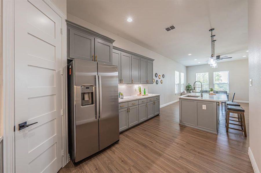 Kitchen featuring gray cabinets, stainless steel refrigerator with ice dispenser, decorative light fixtures, dark wood-style floors, and recessed lighting Kitchen featuring gray cabinets, stainless steel refrigerator with ice dispenser, decorative light fixtures, dark wood-style floors, and recessed lighting