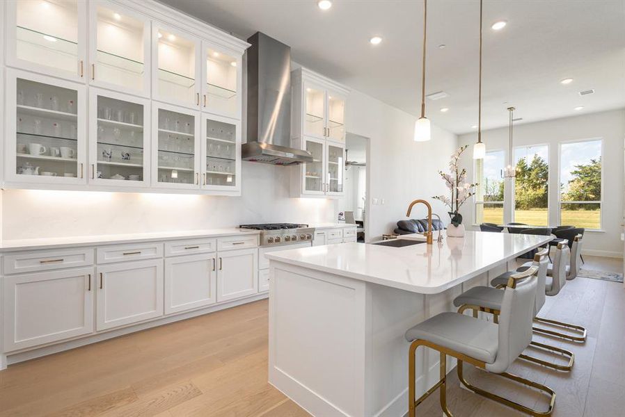 Kitchen featuring white cabinetry, light wood-style floors, wall chimney range hood, a breakfast bar, and pendant lighting