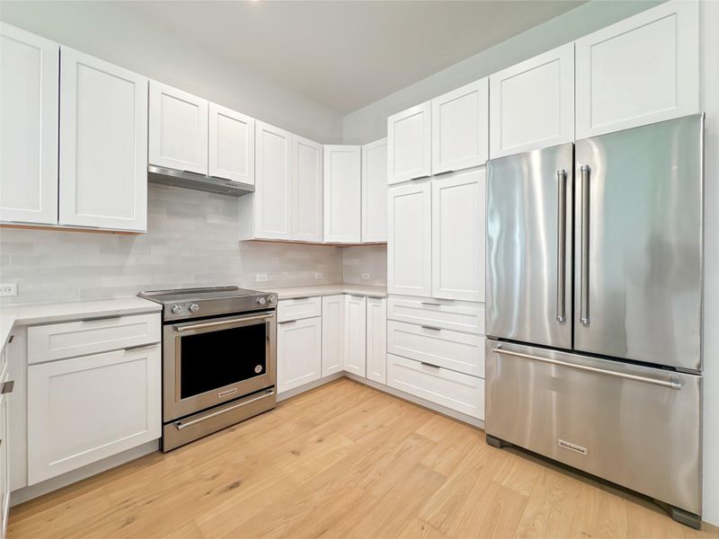 Kitchen featuring stainless steel appliances, under cabinet range hood, light countertops, light wood-style flooring, and white cabinets Kitchen featuring stainless steel appliances, under cabinet range hood, light countertops, light wood-style flooring, and white cabinets