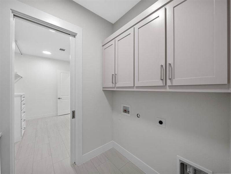 Clothes washing area featuring electric dryer hookup, cabinets, hookup for a washing machine, light tile patterned flooring, and hookup for a gas dryer