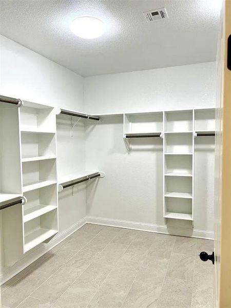 Expansive walk-in closet featuring light-toned tile flooring, built-in shelving, and multiple hanging rods Expansive walk-in closet featuring light-toned tile flooring, built-in shelving, and multiple hanging rods