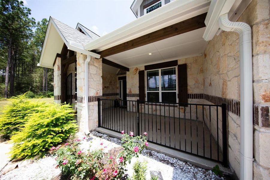 This charming home features a covered stone entryway with a cozy porch, bordered by a well-maintained garden with vibrant flowers and lush greenery, offering a welcoming and serene first impression.