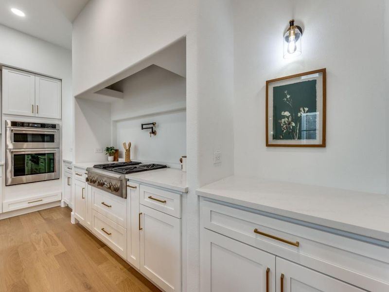 Kitchen with white cabinetry, appliances with stainless steel finishes, light hardwood / wood-style floors, and light stone countertops