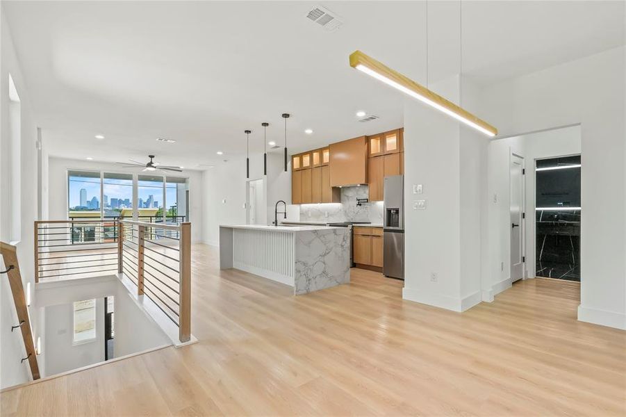 Kitchen featuring glass insert cabinets, brown cabinets, a center island with sink, open floor plan, and pendant lighting