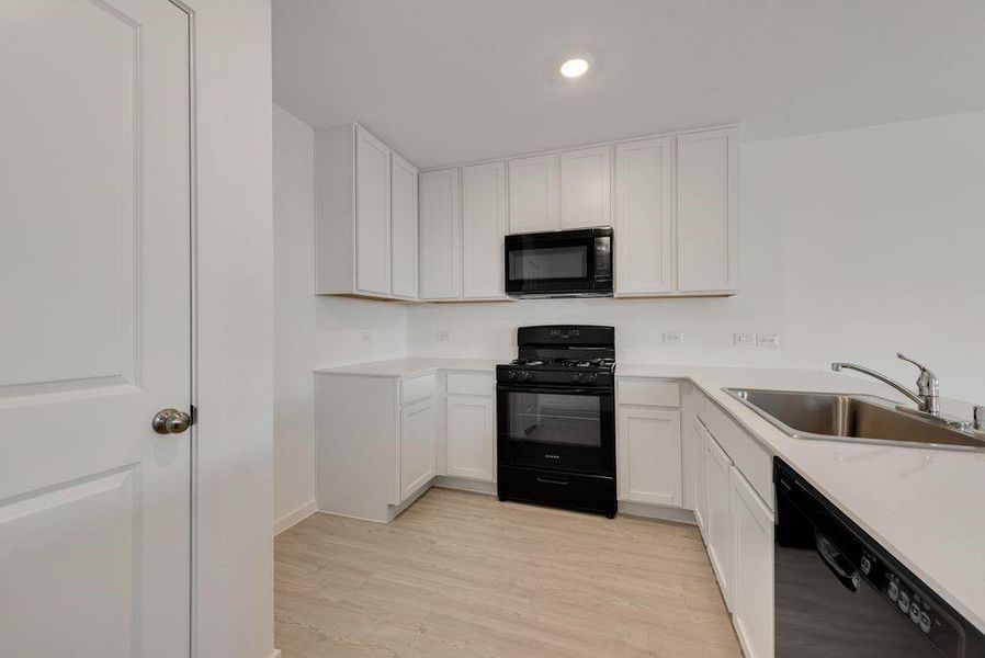 Kitchen featuring black appliances, light wood finished floors, white cabinets, light countertops, and recessed lighting