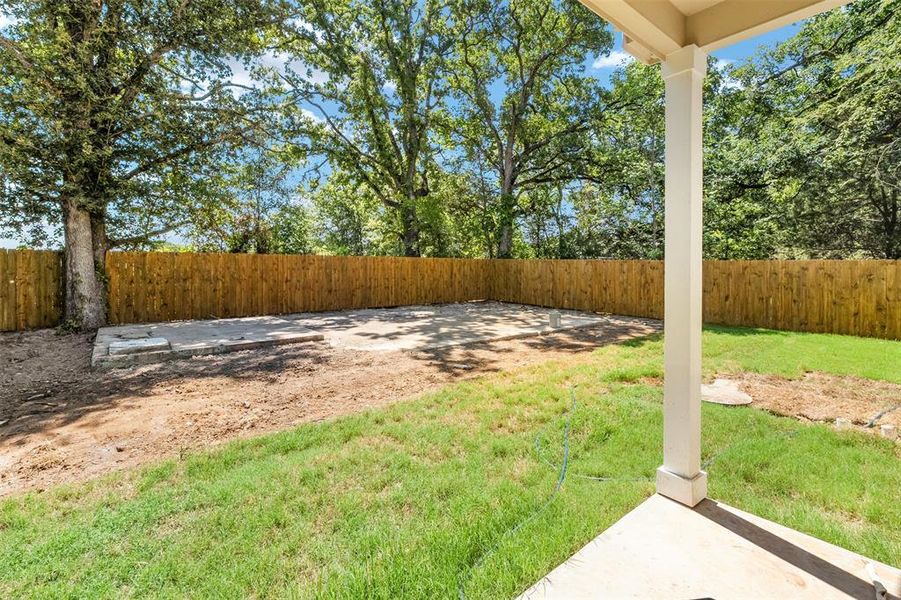 Expansive backyard featuring a newly installed privacy fence, mature trees, a concrete patio area, and a covered porch with a support column Expansive backyard featuring a newly installed privacy fence, mature trees, a concrete patio area, and a covered porch with a support column