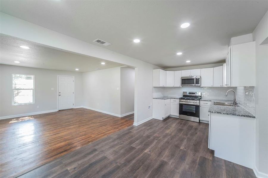 Kitchen with dark wood-type flooring, stainless steel appliances, white cabinets, stone countertops, and sink