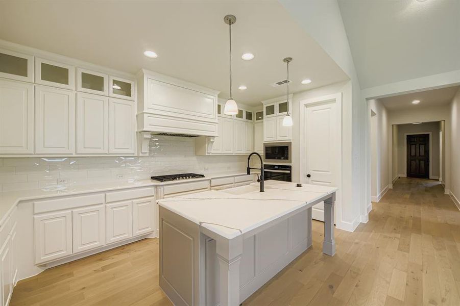 Kitchen featuring decorative backsplash, a breakfast bar, light wood-style flooring, glass insert cabinets, and recessed lighting