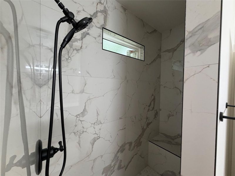 Marble-clad shower with a sleek, modern fixture and a convenient built-in bench.