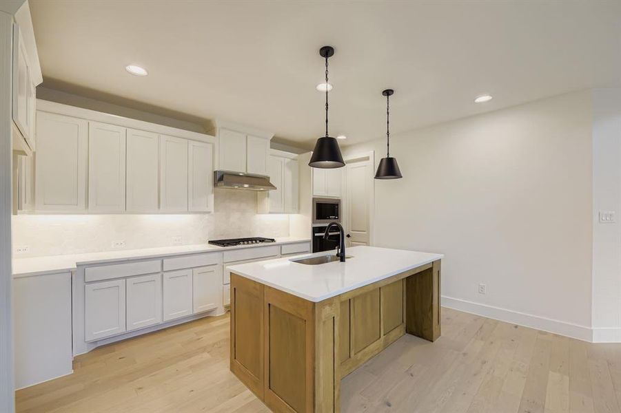 Kitchen with white cabinetry, backsplash, light wood-type flooring, decorative light fixtures, and brown cabinets Kitchen with white cabinetry, backsplash, light wood-type flooring, decorative light fixtures, and brown cabinets