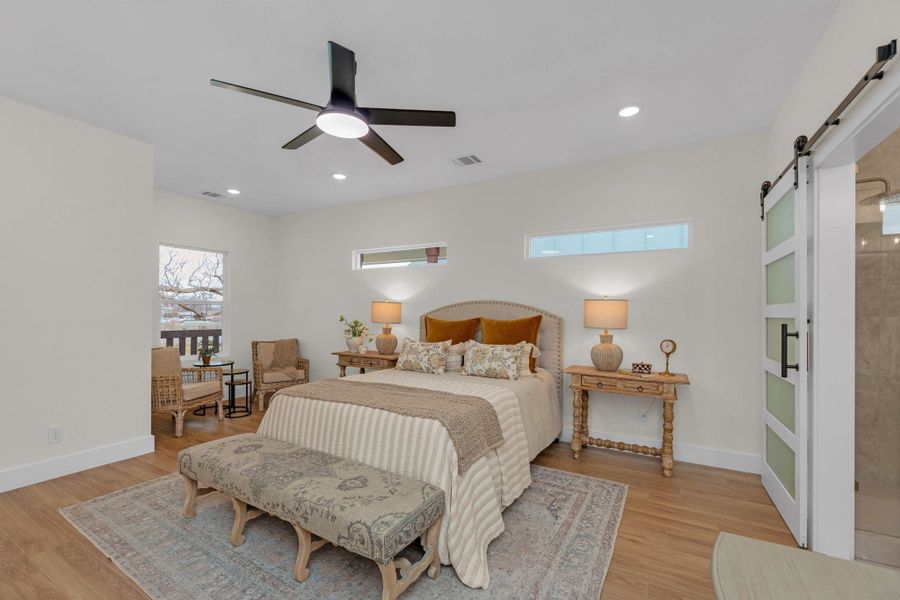 Bedroom featuring a barn door, Optimax Performance Azalea Oak Hybrid Resilient Flooring that is a wood based.  Ceiling fan and recessed lighting.