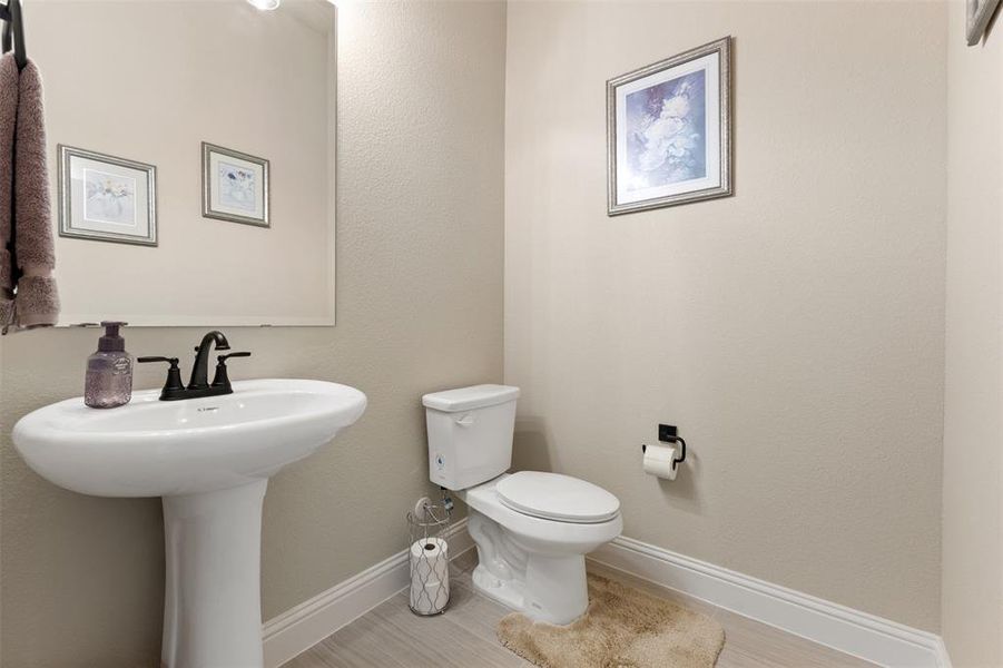 Pedestal sink with a matte black faucet, wall-mounted mirror, and light wood-finish flooring Pedestal sink with a matte black faucet, wall-mounted mirror, and light wood-finish flooring