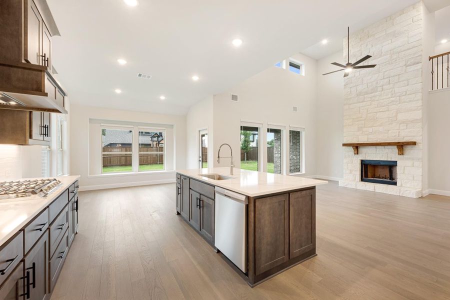Open-concept kitchen with dark wood island, quartz countertops, and stone fireplace in adjoining living area Open-concept kitchen with dark wood island, quartz countertops, and stone fireplace in adjoining living area