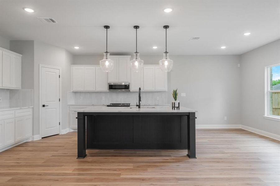 Kitchen featuring decorative light fixtures, light hardwood / wood-style floors, white cabinets, and backsplash