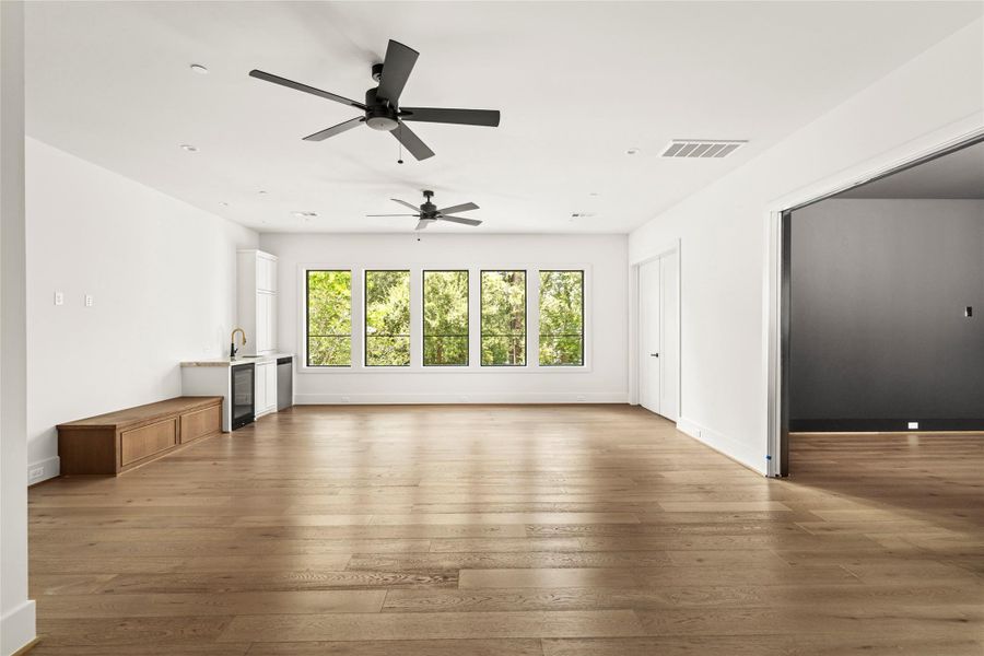 Expansive game room with warm wood flooring, a built-in wet bar, large windows, and flexible space for entertaining.