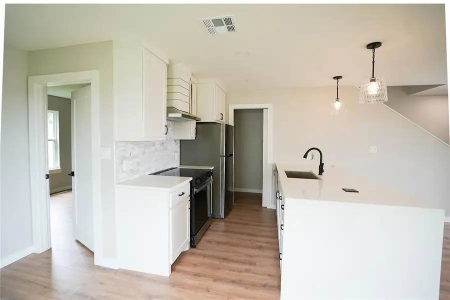 Kitchen with stainless steel appliances, under cabinet range hood, light wood-style flooring, and white cabinetry