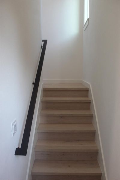 Clean lines and light wood steps define this bright, ascending stairway with a sleek black handrail.