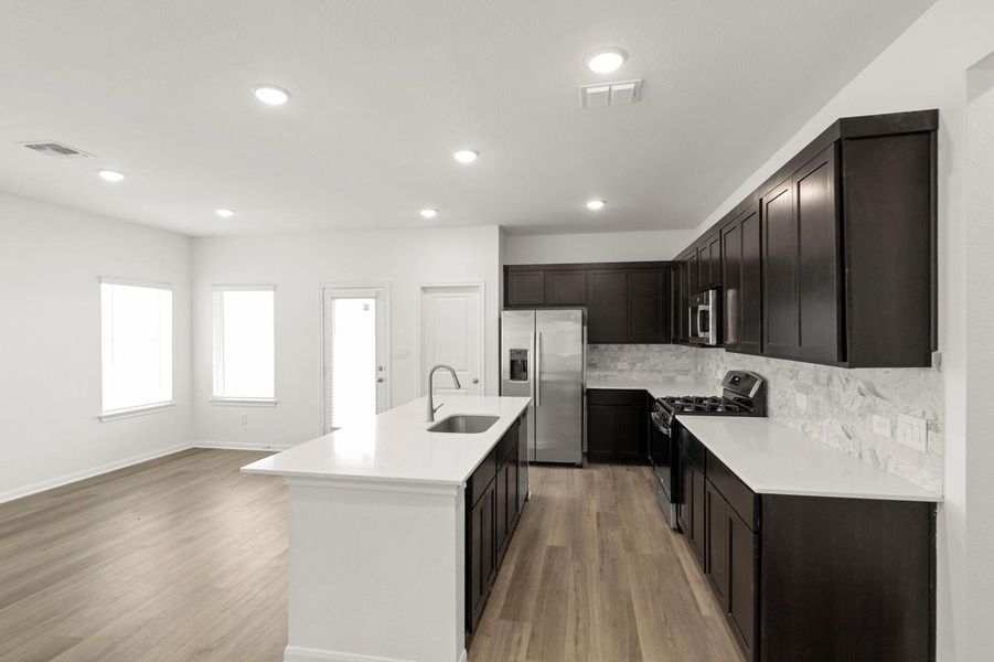 Kitchen with stainless steel appliances, light wood-style flooring, a kitchen island with sink, light stone counters, and recessed lighting