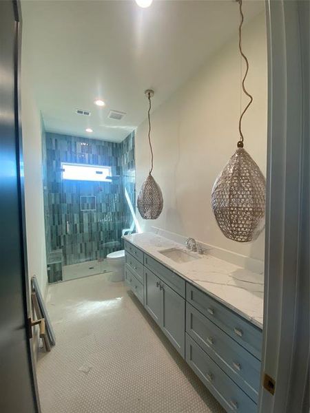 Bathroom featuring toilet, vanity, a tile shower, and tile walls