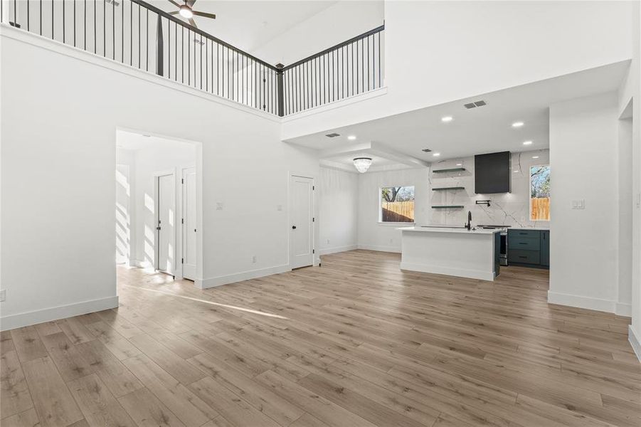 Unfurnished living room with light wood-type flooring, recessed lighting, a towering ceiling, and ceiling fan