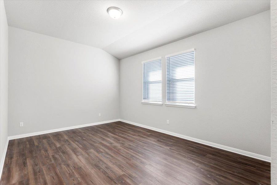 Empty room featuring dark wood-style floors, vaulted ceiling, and baseboards