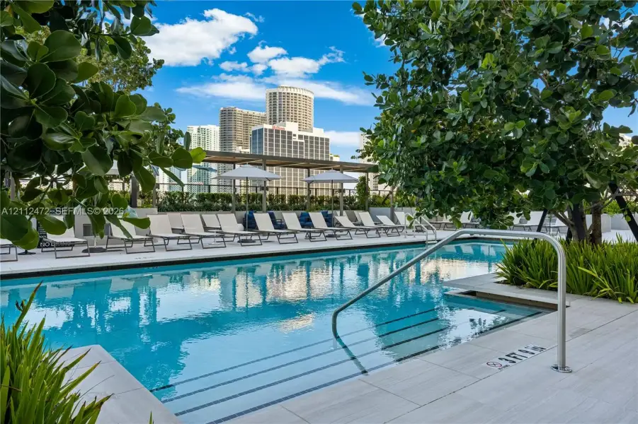 Swimming pool with integrated steps, tile decking, metal handrails, and a pergola structure