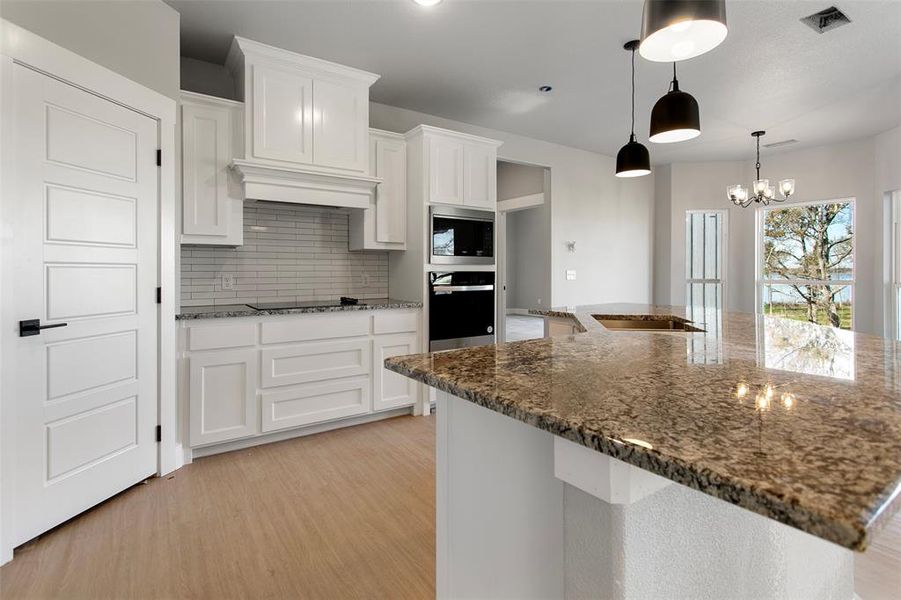 Kitchen featuring white cabinets, stainless steel appliances, decorative light fixtures, and light hardwood / wood-style floors