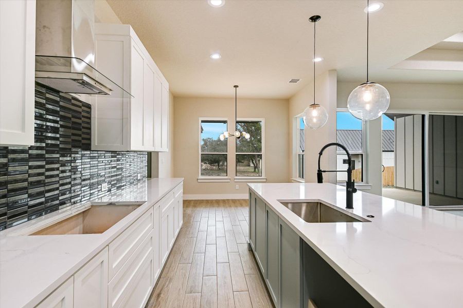 Kitchen featuring two tone cabinetry, light stone counters, light wood finished floors, a chandelier, and black electric cooktop