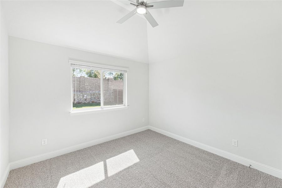 Empty bedroom with vaulted ceiling, ceiling fan, carpet flooring, and a single window with backyard view Empty bedroom with vaulted ceiling, ceiling fan, carpet flooring, and a single window with backyard view