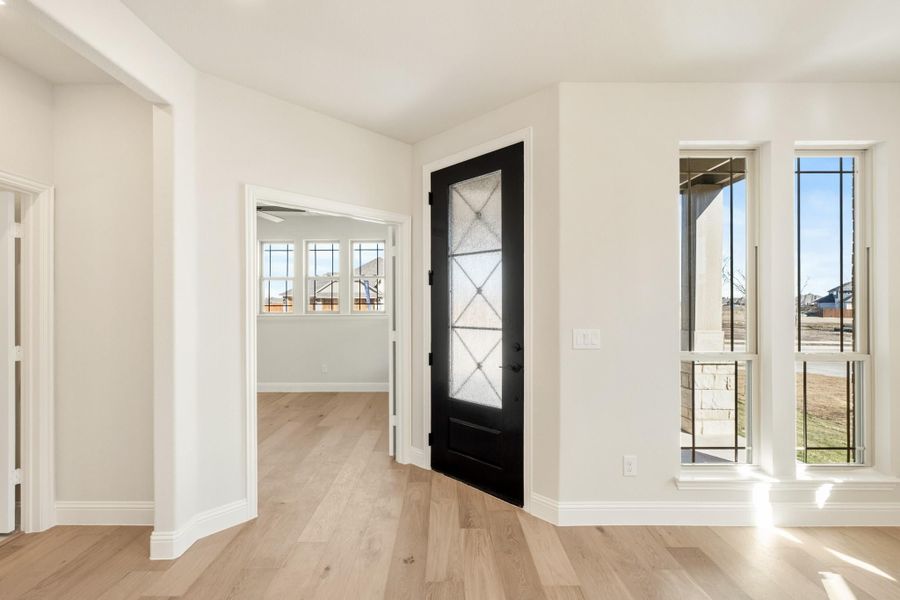 Bright home entryway with black glass-panel front door, white walls, and light hardwood floors
