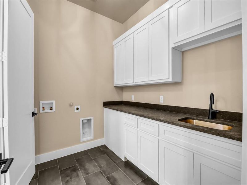 Clothes washing area featuring electric dryer hookup, cabinets, dark tile patterned flooring, sink, and washer hookup