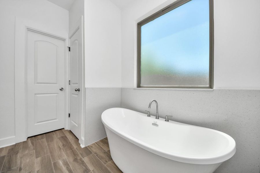 This bathroom features a modern freestanding bathtub, a frosted window for privacy, creating a sleek and relaxing space.