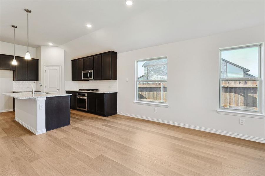 Kitchen featuring decorative backsplash, light hardwood / wood-style flooring, appliances with stainless steel finishes, and an island with sink