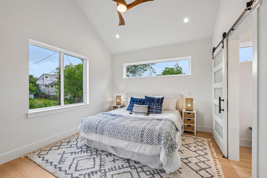 Vast windows illuminate this primary bedroom, featuring vaulted ceilings with a fan.