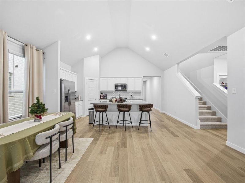 Kitchen with white cabinetry, a breakfast bar, a kitchen island with sink, decorative backsplash, and light wood-style flooring