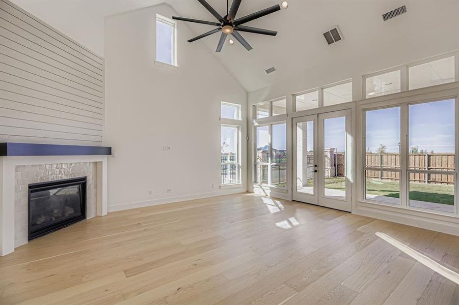Unfurnished living room with high vaulted ceiling, a tiled fireplace, ceiling fan, light wood finished floors, and french doors Unfurnished living room with high vaulted ceiling, a tiled fireplace, ceiling fan, light wood finished floors, and french doors
