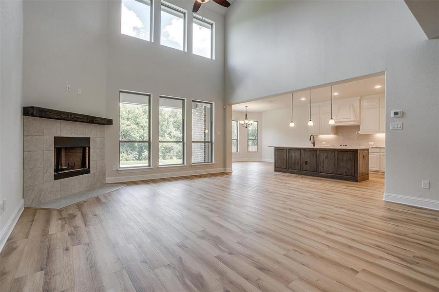 Unfurnished living room featuring light hardwood / wood-style flooring, sink, a tile fireplace, a high ceiling, and ceiling fan with notable chandelier