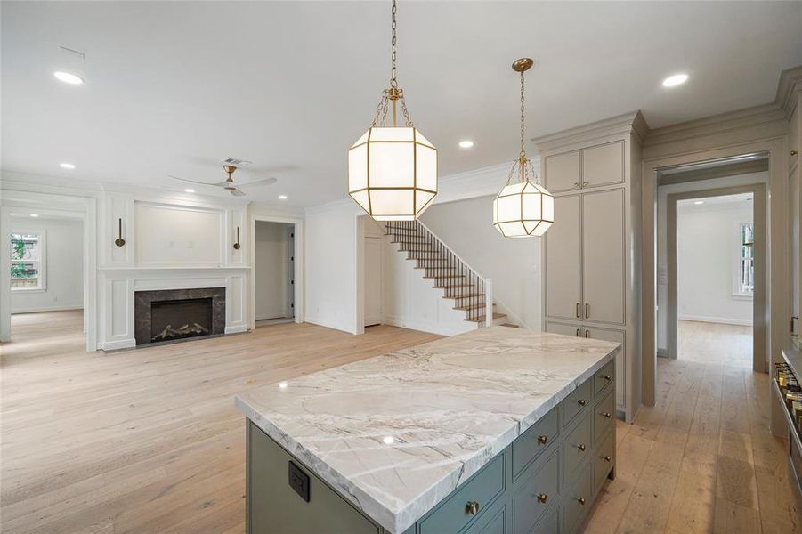 Elegant open-concept space featuring art deco lighting, a kitchen island opens to a living room with a cozy gas fireplace and hardwood floors.