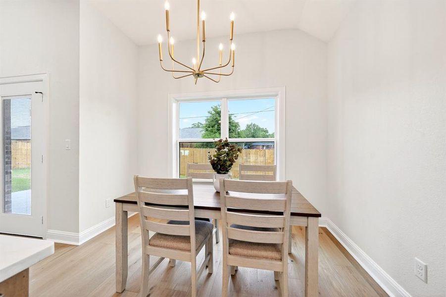Dining area with vaulted ceiling, wood-finish flooring, and a modern gold-tone chandelier