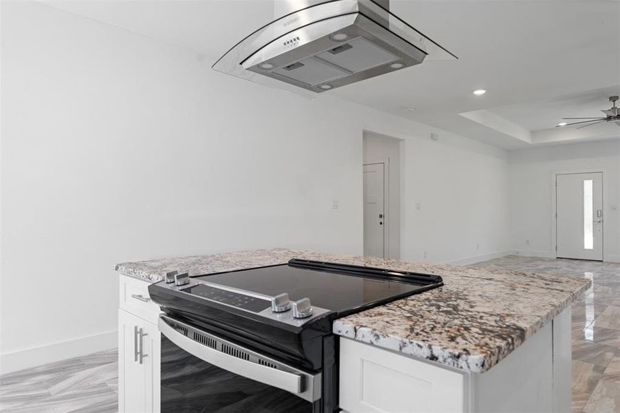 Kitchen with white cabinets, ceiling fan, light stone countertops, and stainless steel electric stove