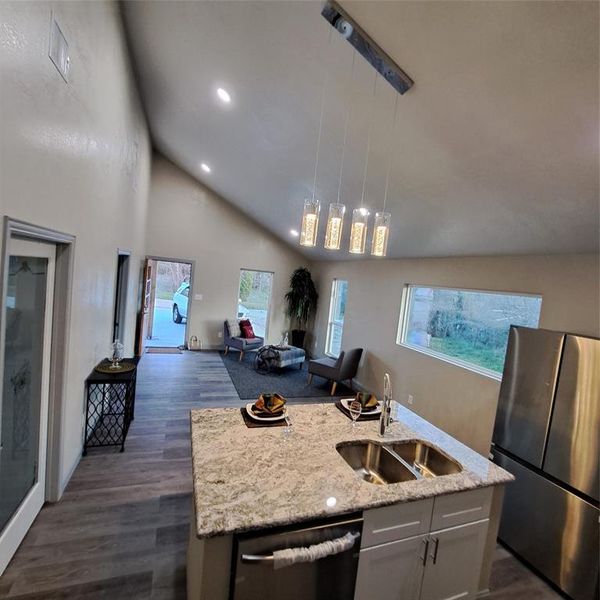 Kitchen featuring stainless steel fridge, an island with sink, dishwashing machine, decorative light fixtures, and sink