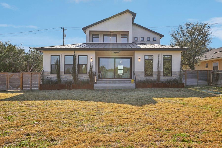 Rear view of house featuring a standing seam roof, stone siding, a gate, and stucco siding
