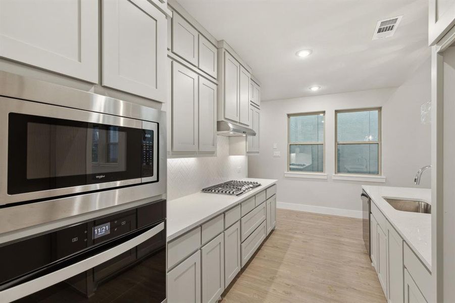 Kitchen featuring backsplash, stainless steel appliances, light hardwood / wood-style floors, white cabinetry, and sink